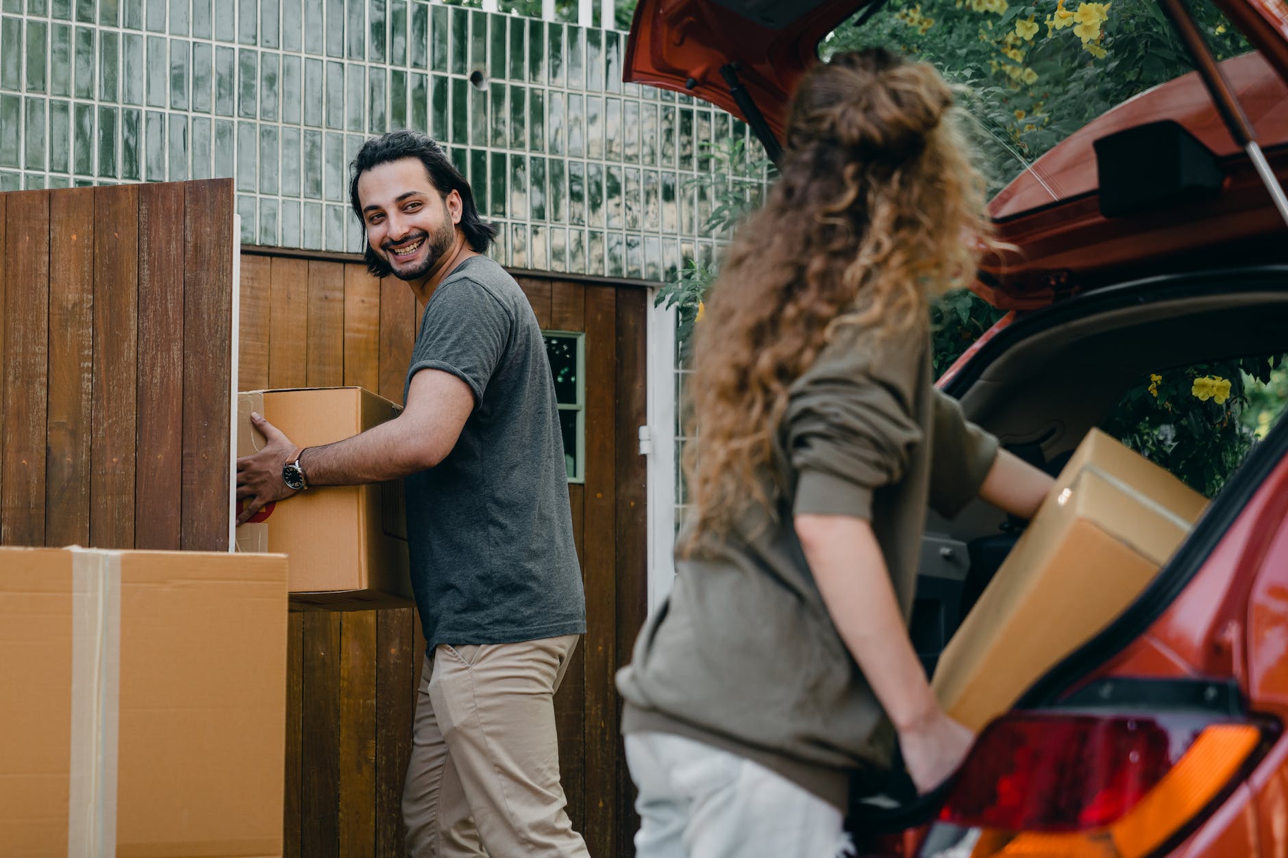 happy couple unloading automobile while moving apartment in summer day